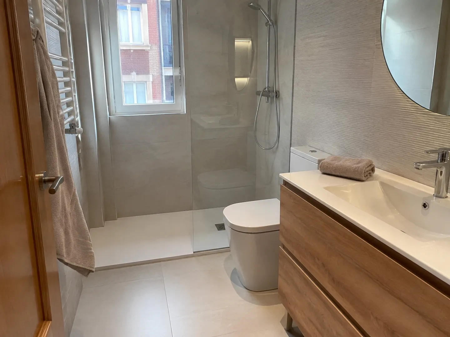 Distribución de un baño con ducha y lavabo de madera Baño con ducha a ras de suelo, mampara transparente y espejo redondo sobre el lavabo